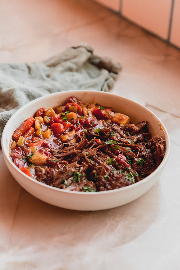 A bowl of Italian pot roast on the counter with a napkin being ready to be consumed.