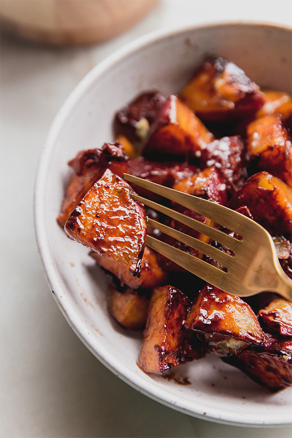 A fork taking a candied Japanese sweet potato out of the serving bowl.