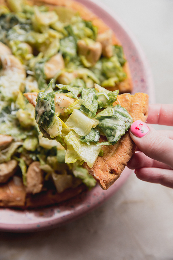 A piece of chicken caesar salad pizza being taken from the pizza.