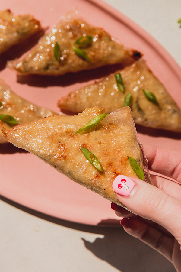 A hand picking up a crab rangoon off of a serving platter.