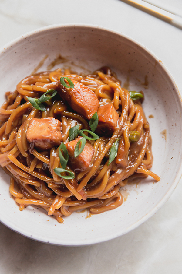 A bowl with a serving of baked honey garlic chicken noodle dish ready to be eaten.