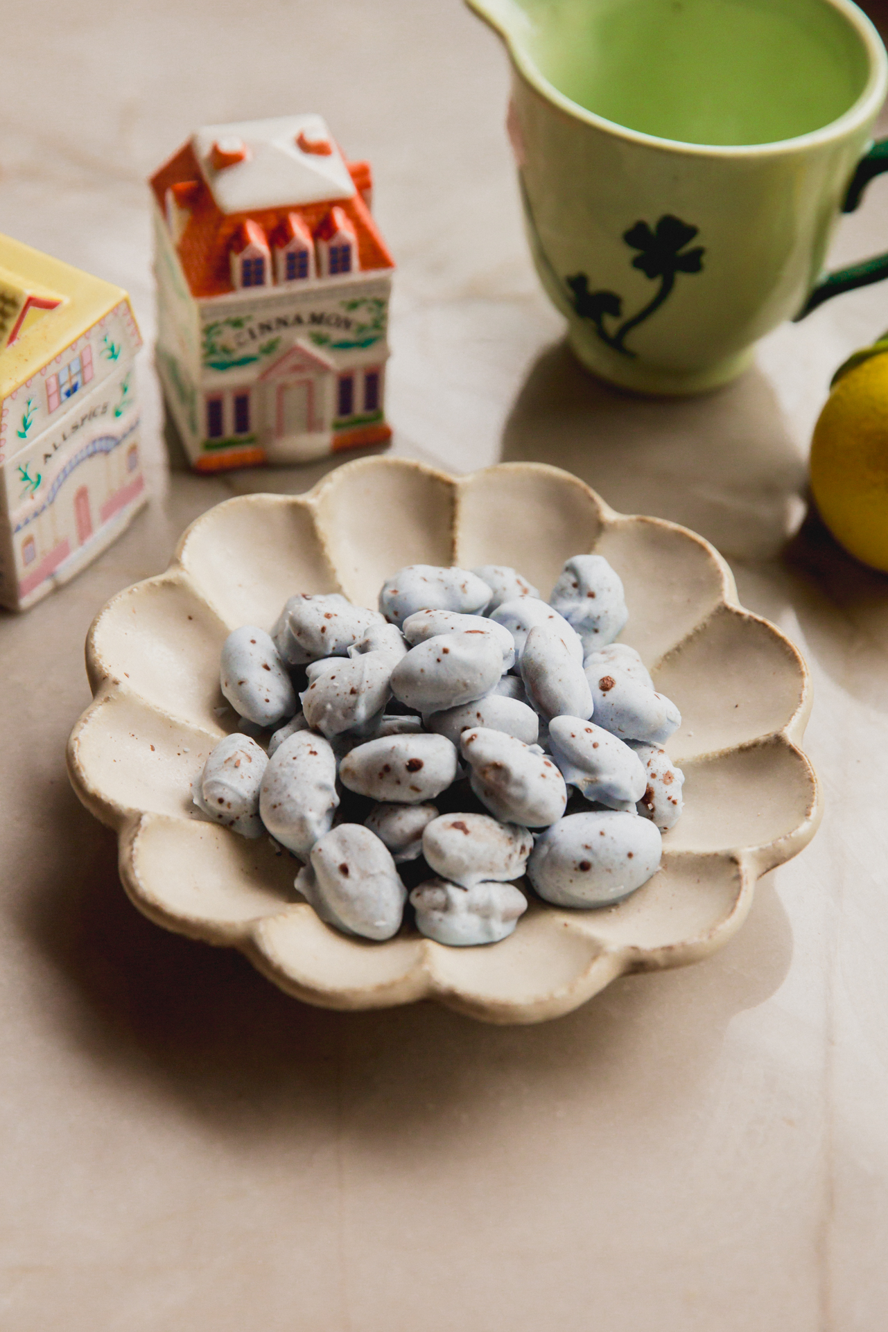 Blue chocolate covered almonds with brown speckles in a bowl with spring kitchen decor in the background.