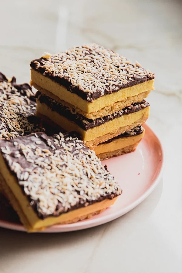 Lemon smores bars topped with toasted coconut, stacked on a pink plate.