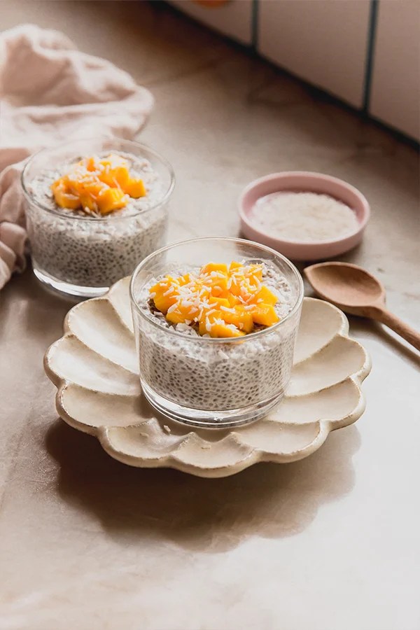 Mango sticky rice chia pudding topped with diced mango and coconut, with another bowl in the background and a small wooden spoon.