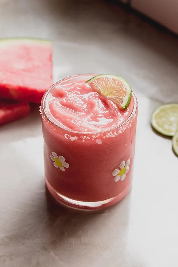 Frozen watermelon margarita mocktail in a glass with a salted rim and topped with a slice of lime.