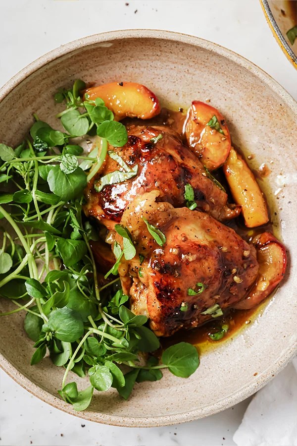 Balsamic chicken thighs and peached served with greens in a large bowl.