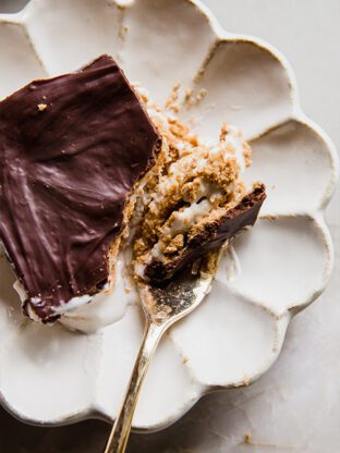 A slice of eclair cake on a plate, with a fork cutting a slice to show the layers of the cake.