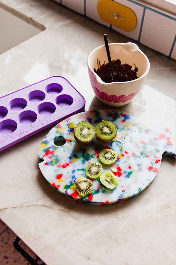 Sliced kiwi on a cutting board with melted chocolate in a bowl.