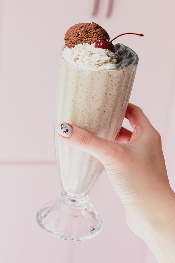 Ninja creami milkshake topped with whipped cream, a cookie and a cherry, being held in a milkshake cup.