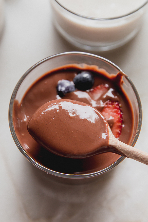 Chocolate pudding in a glass cup topped with berries and being scooped with a wooden spoon.
