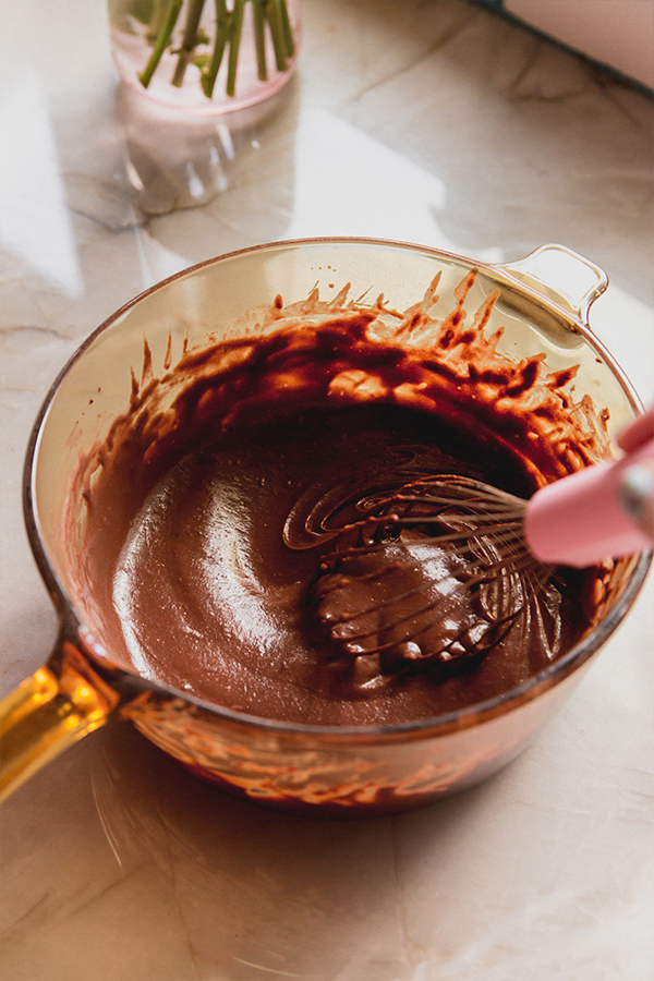 Fully cooked chocolate pudding being whisked in a glass pot.