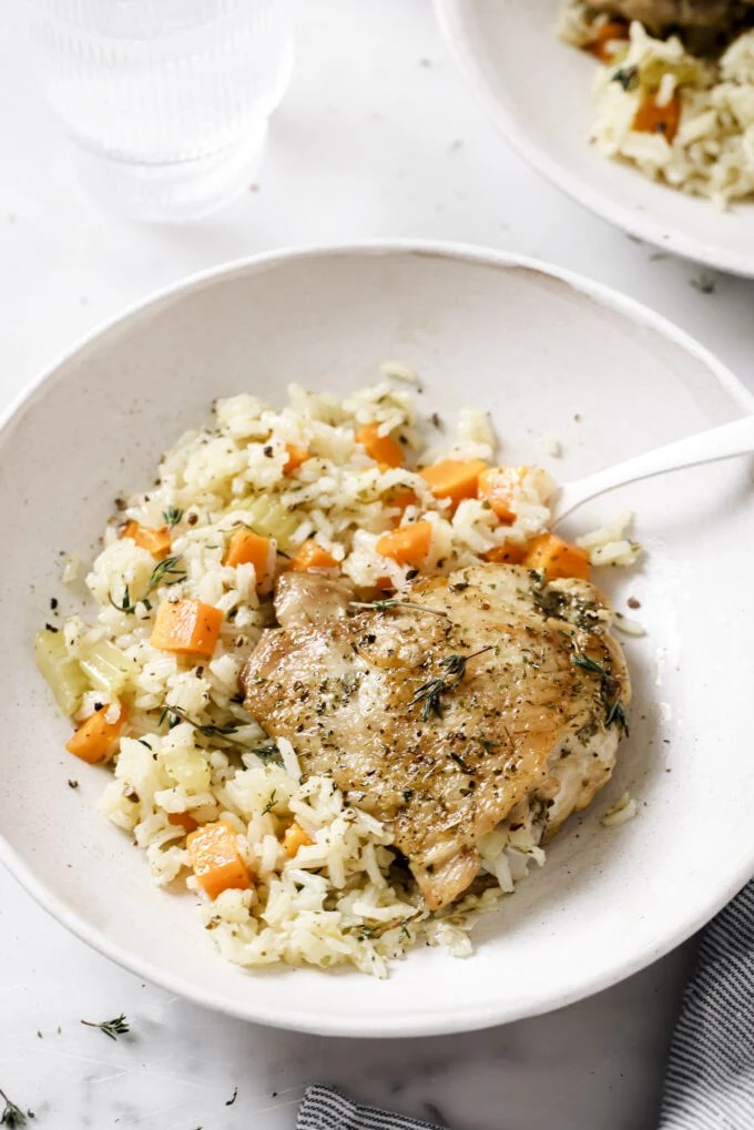 One pot baked chicken and rice in a white bowl topped with herbs.