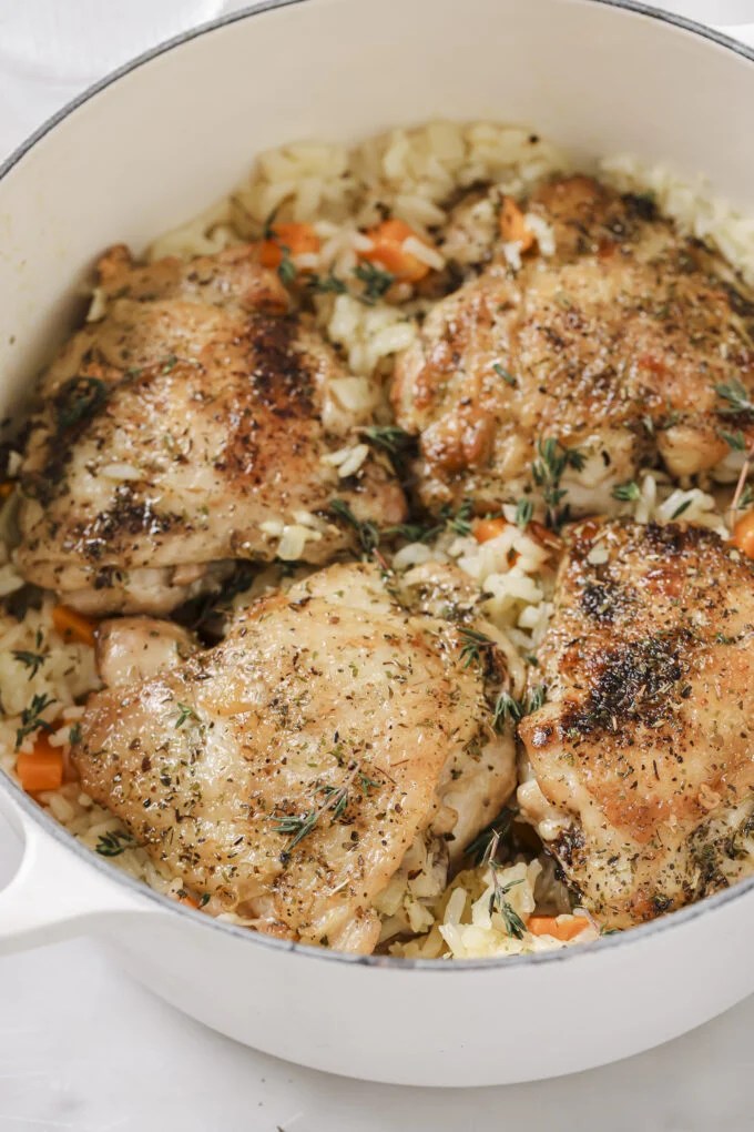 One pot baked chicken and rice in a large white pot, topped with fresh herbs.