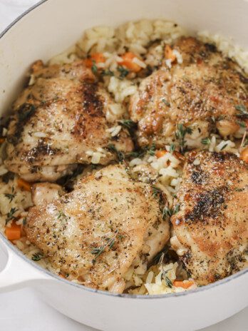 One pot baked chicken and rice in a large white pot topped off with fresh herbs.