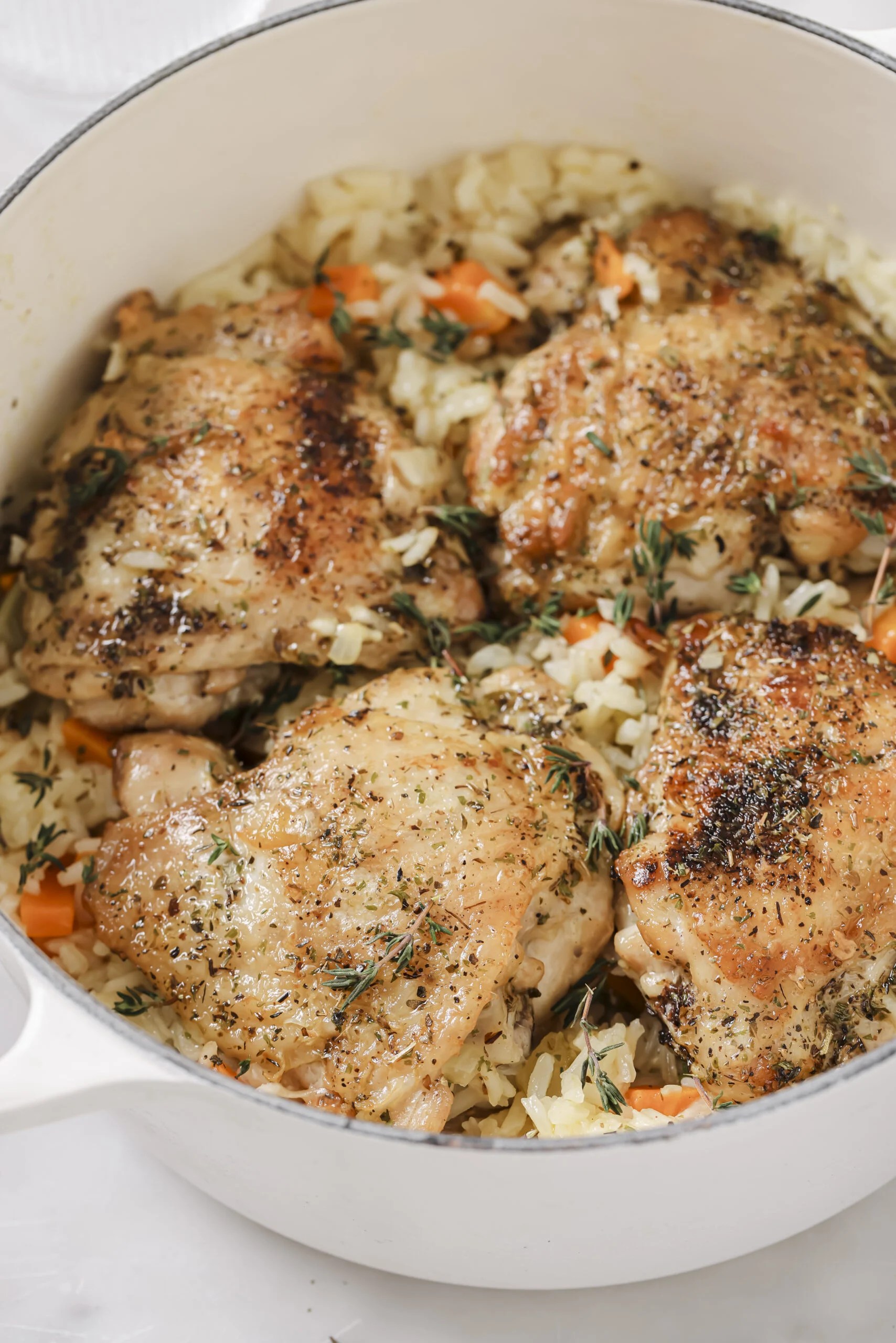 One pot baked chicken and rice in a large white pot topped off with fresh herbs.