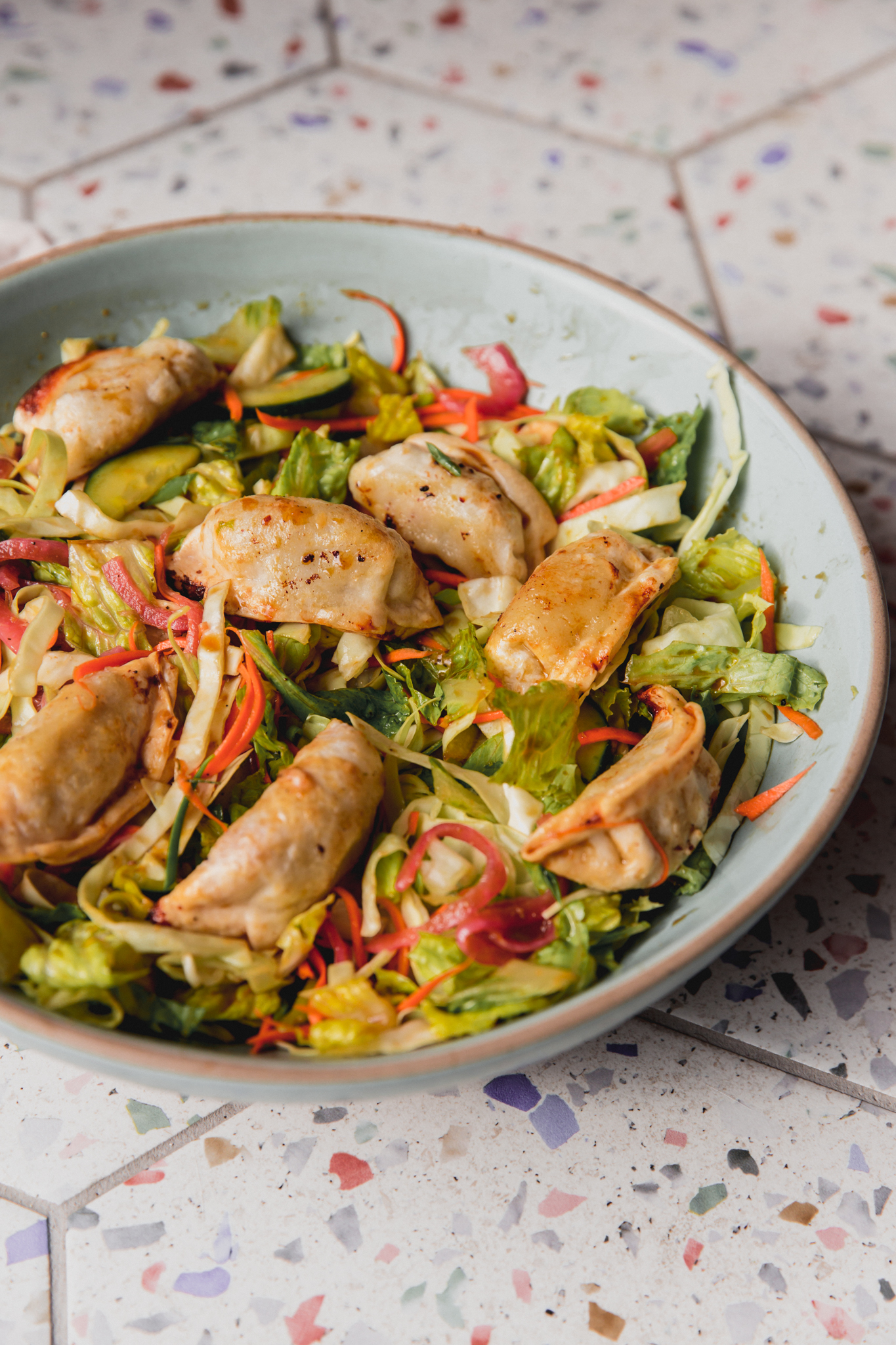 Dumping salad in a large bowl with veggies and dumplings.