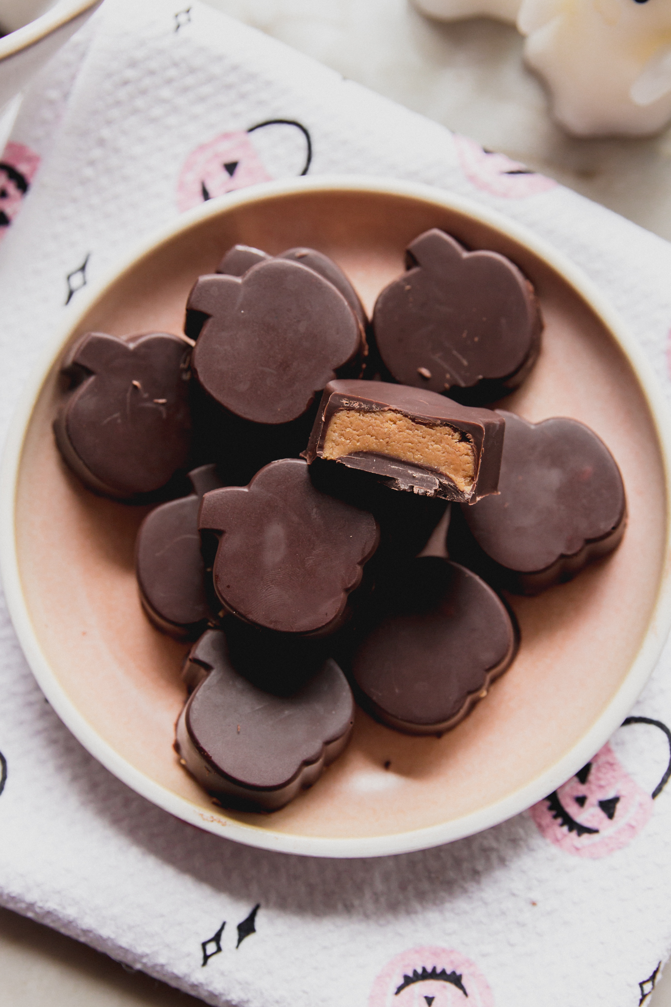 Almond butter cups shapes like pumpkins on a pink plate, with a bite taken from one.