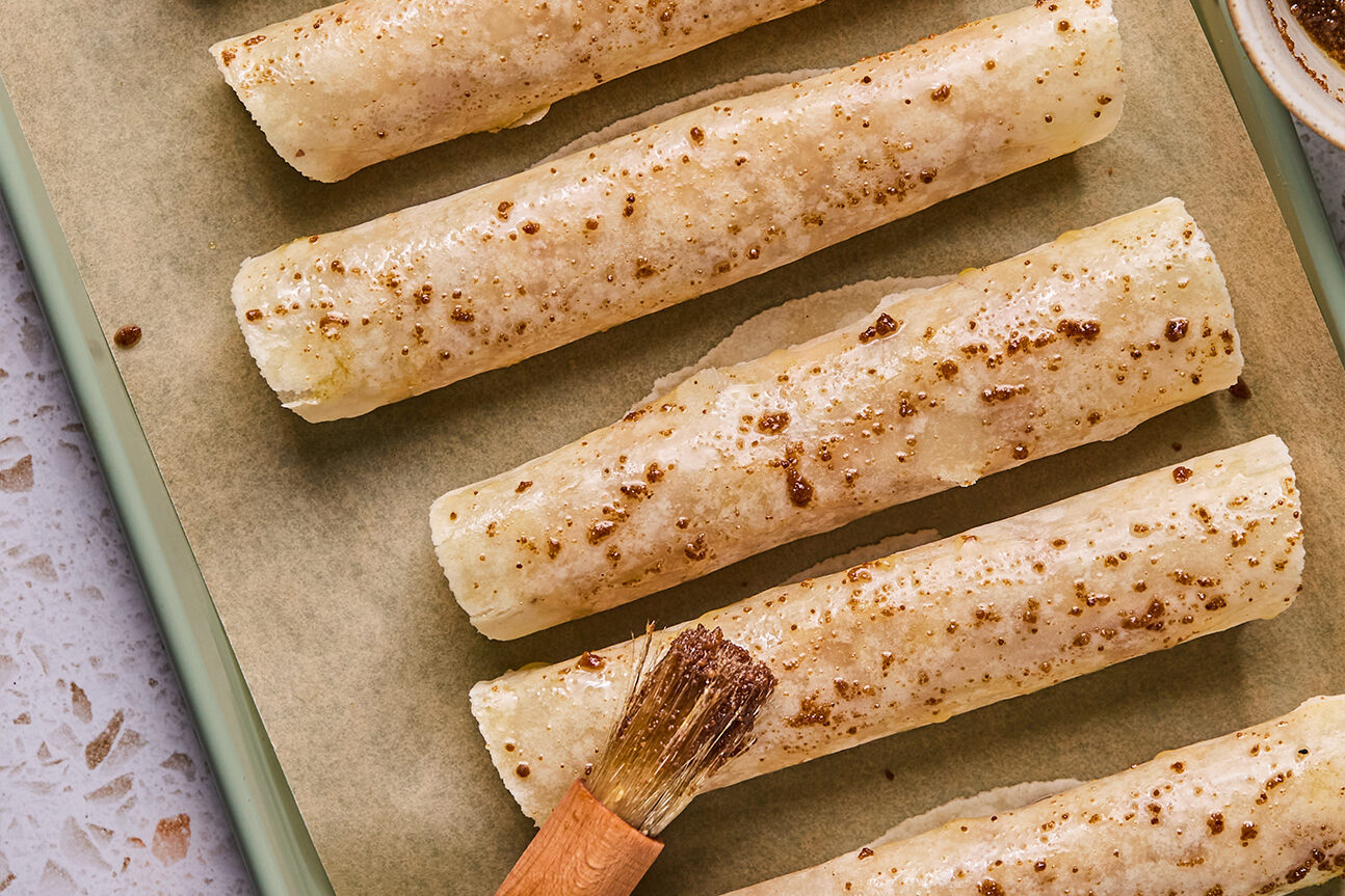 Apple pie roll ups rolled on a baking sheet and brushed with ghee and coconut sugar.