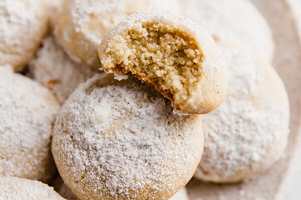Wedding cookies stacked and topped with powdered sugar, with a bite taken out of one on top.