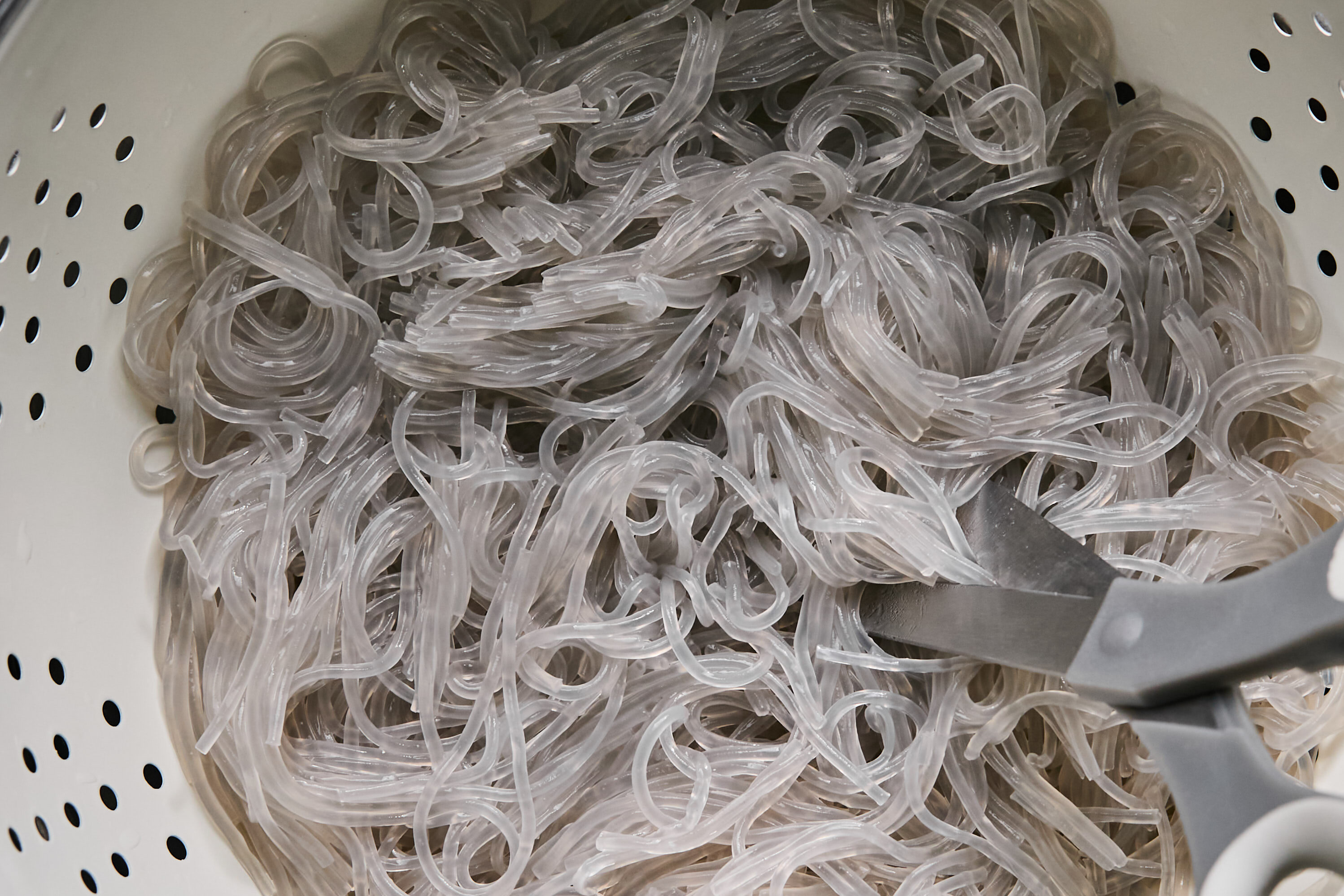 Scissors in a colander with glass noodles.