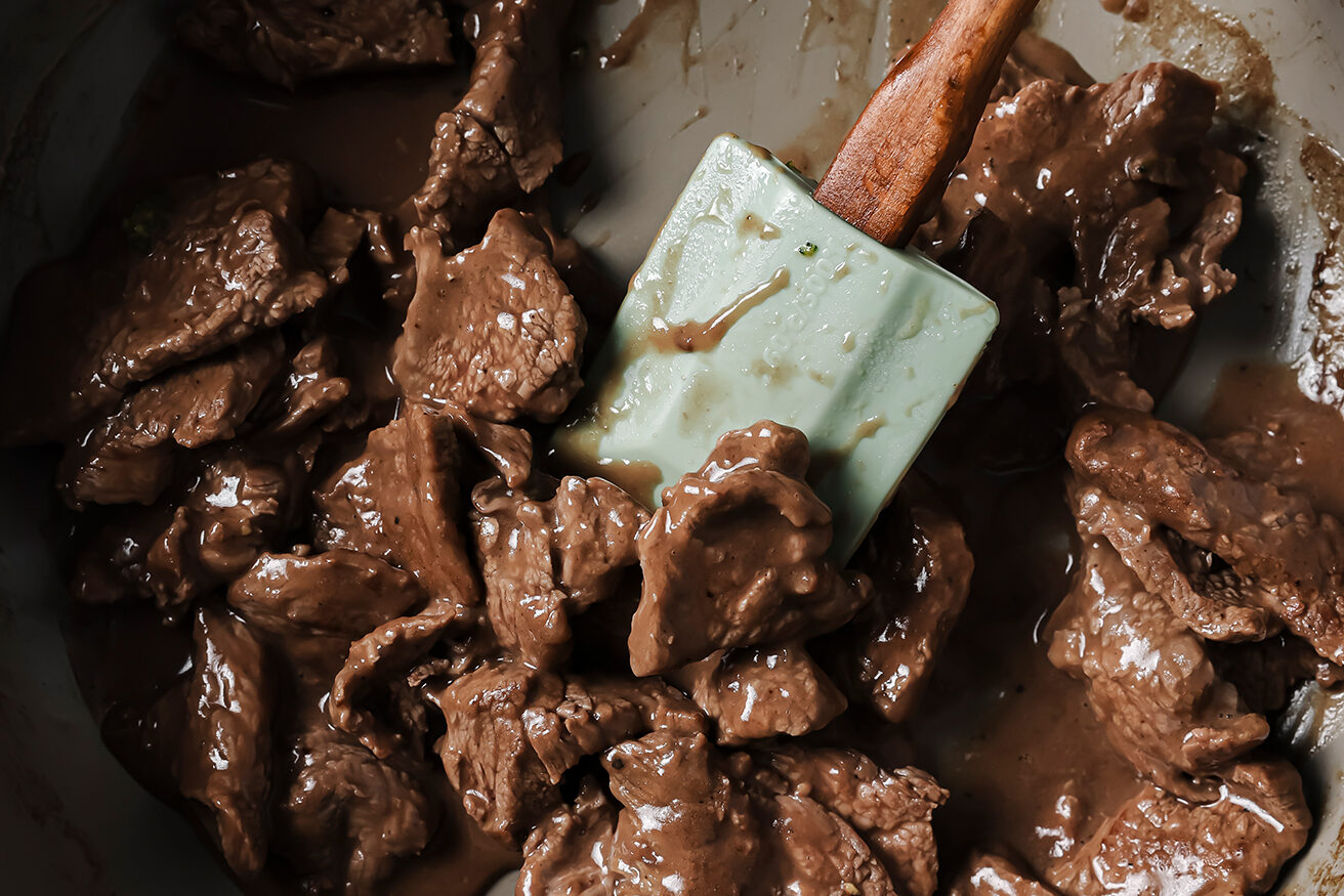 Mongolian beef cooking in a pan with sauce.