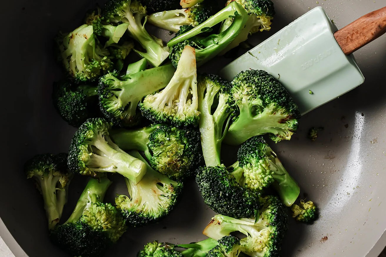 Broccoli florets being cooked in a pan with a spatula.