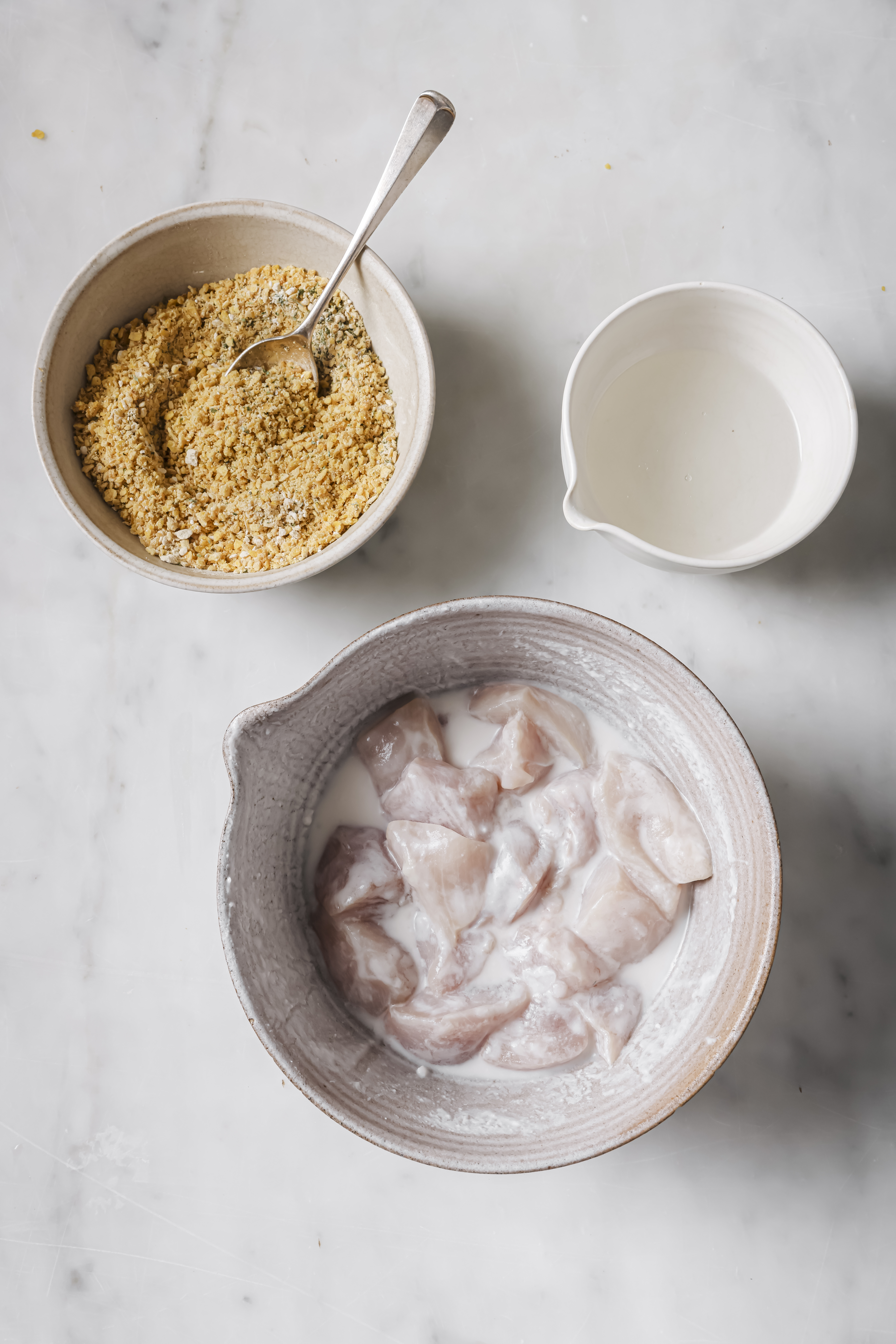 separate bowls of chicken mixture, ground plantain chips, and coconut oil