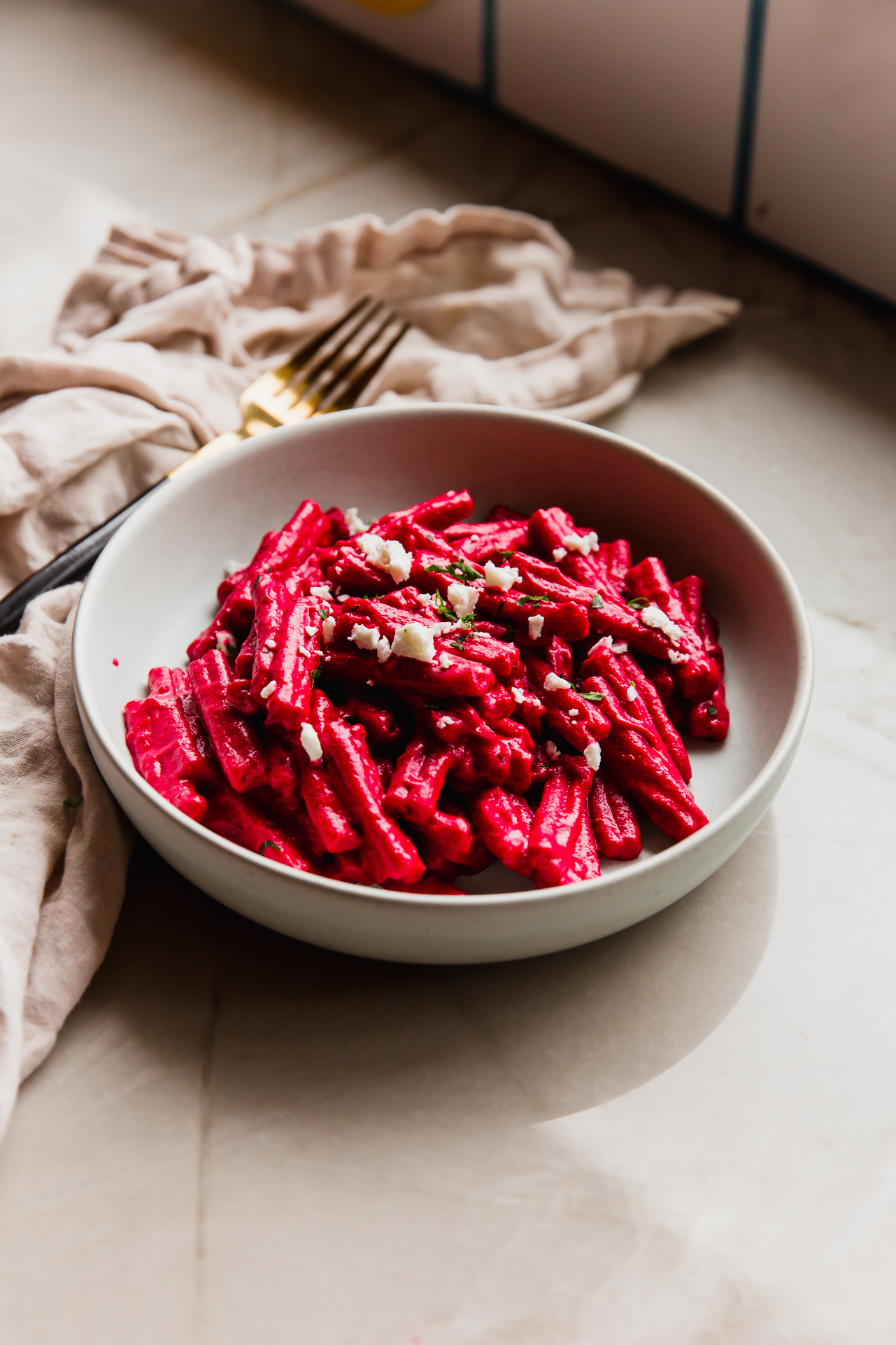 Beet pasta in a bowl topped with feta cheese and parsley.