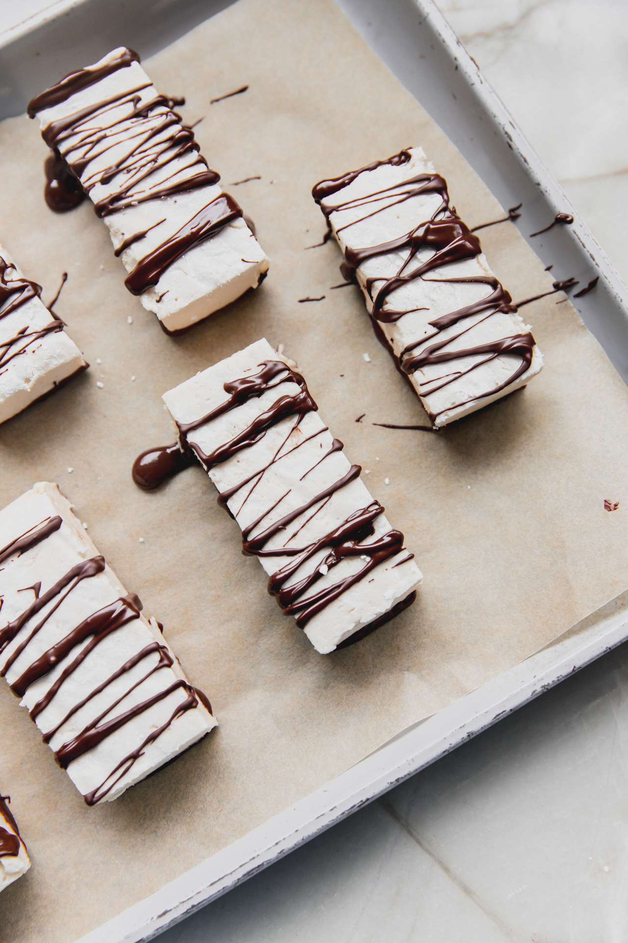 marshmallow protein bars with chocolate drizzle on a parchment lined baking sheet