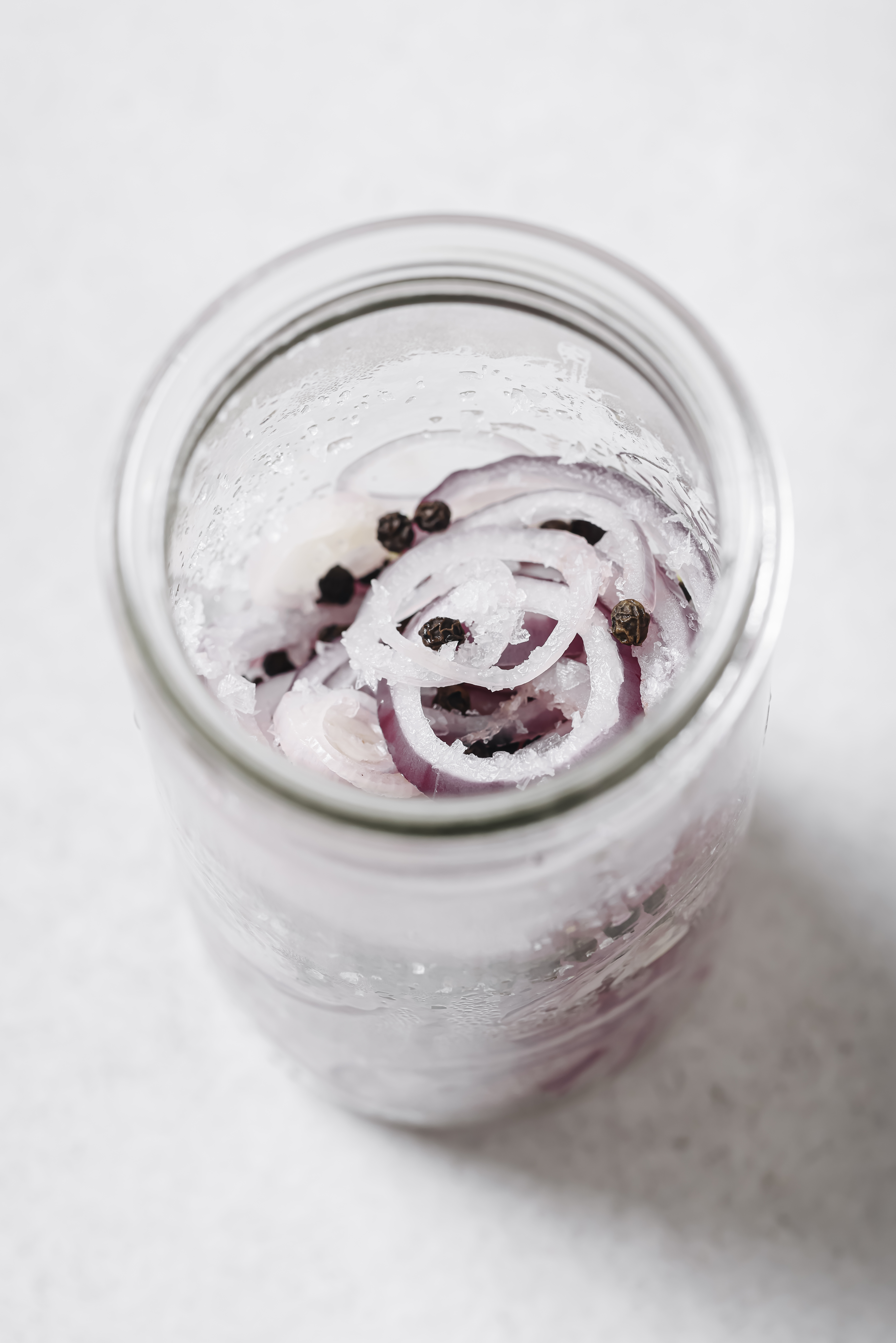 red onion slices in a jar with peppercorns and salt