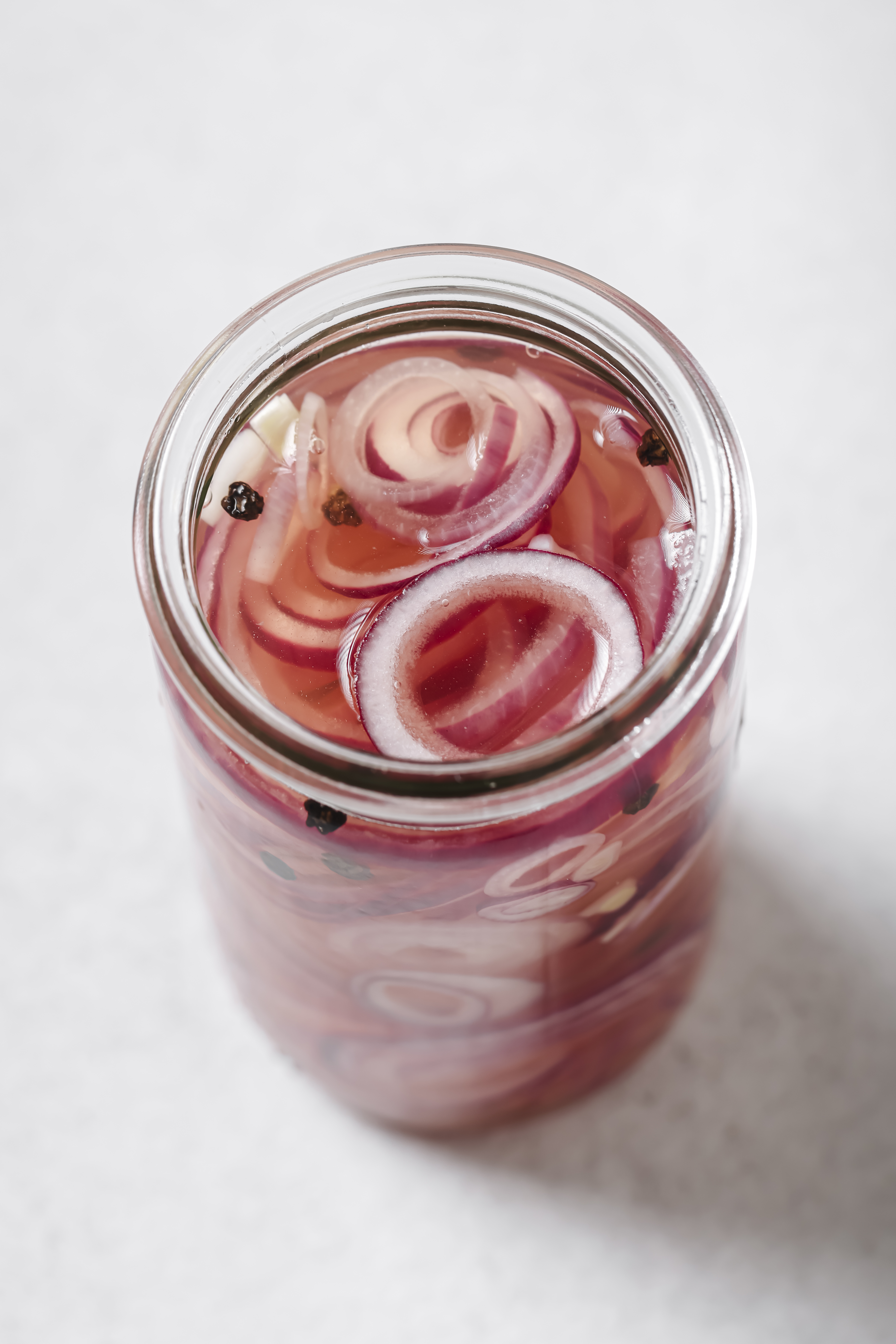 red onion slices in a jar with peppercorns and salt, submerged in apple cider vinegar