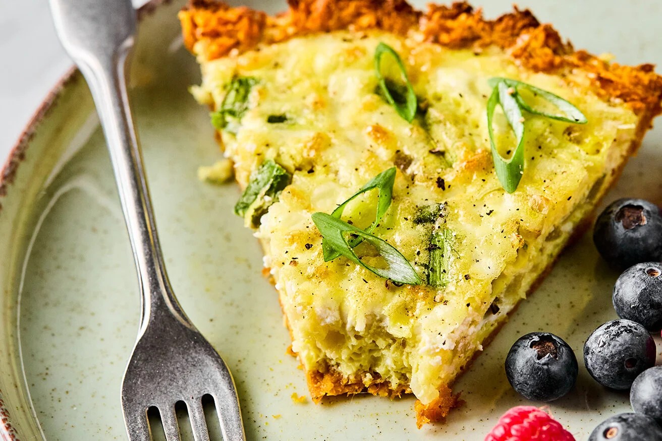 A slice of sweet potato quiche with a bite taken out of it and berries on the side.