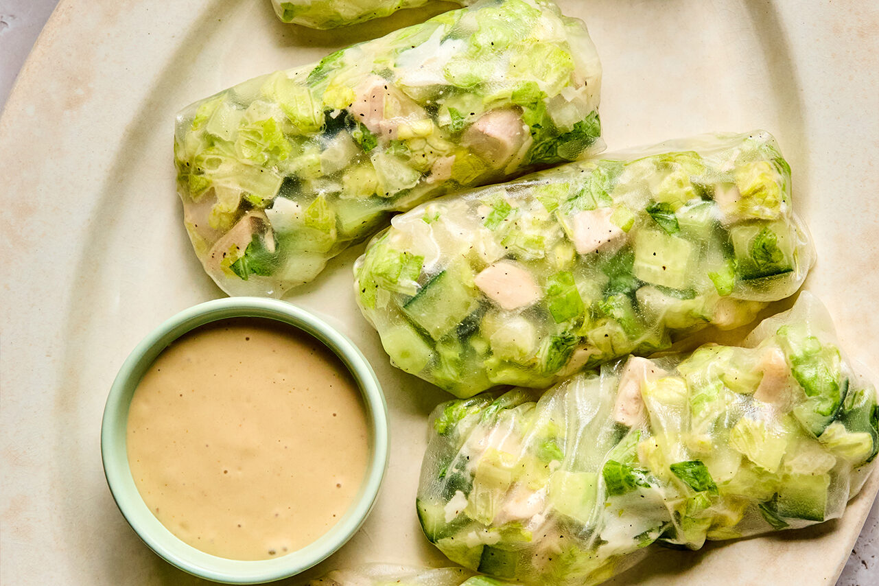 A platter with 5 chicken caesar salad rice paper rolls and caesar dressing for dipping.
