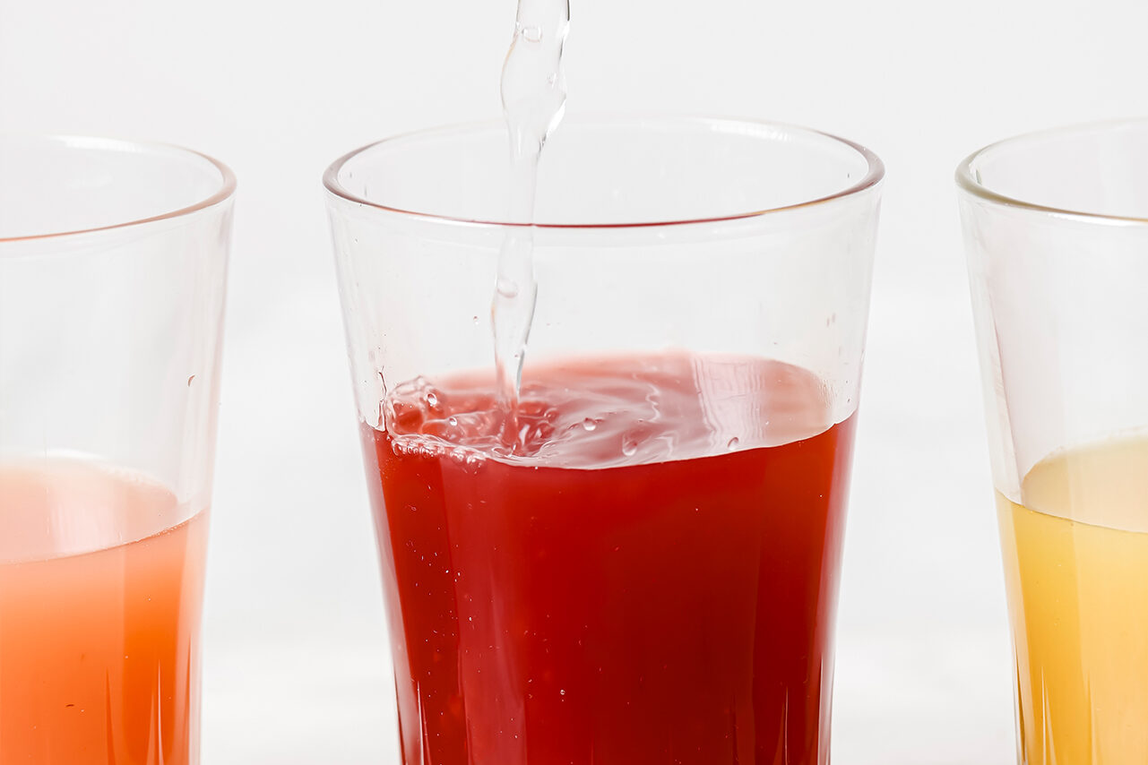A glass filled with an apple cider vinegar shot and water being poured into it.