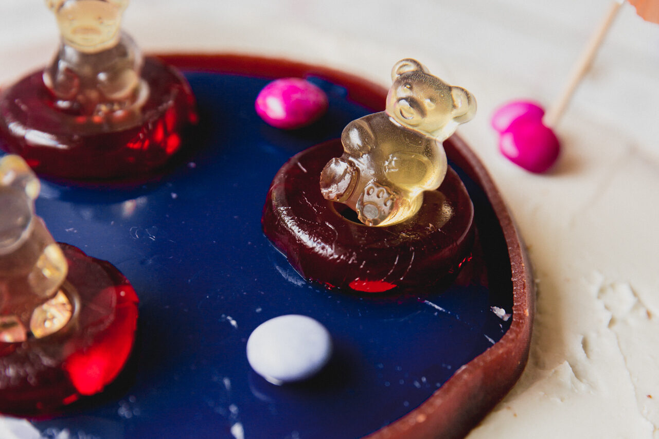 Swimming pool cake topped off with a gummy bears sitting up in a ring gummy.