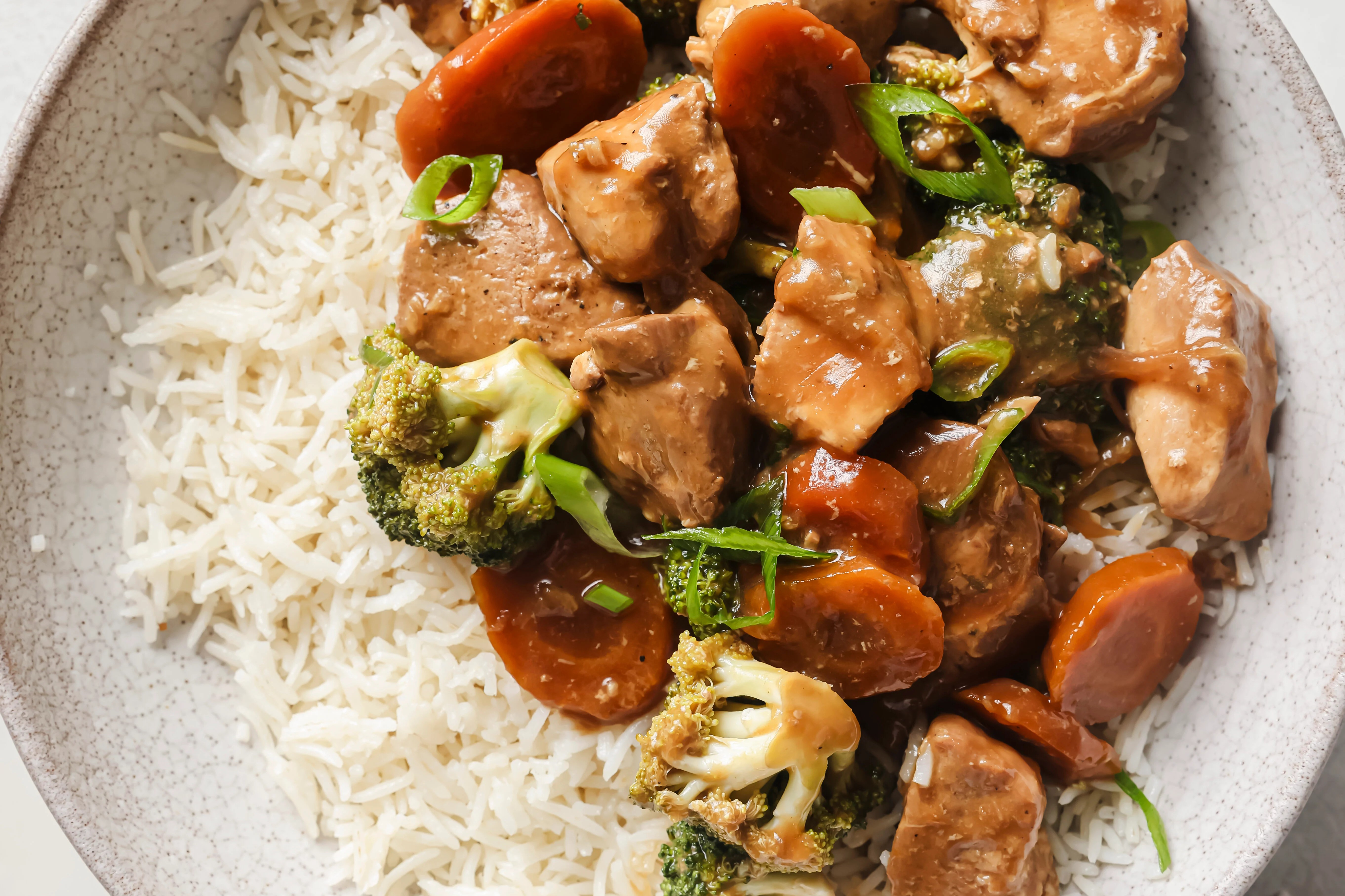 Fully cooked chicken and broccoli with a side of rice, topped with chopped green onions.