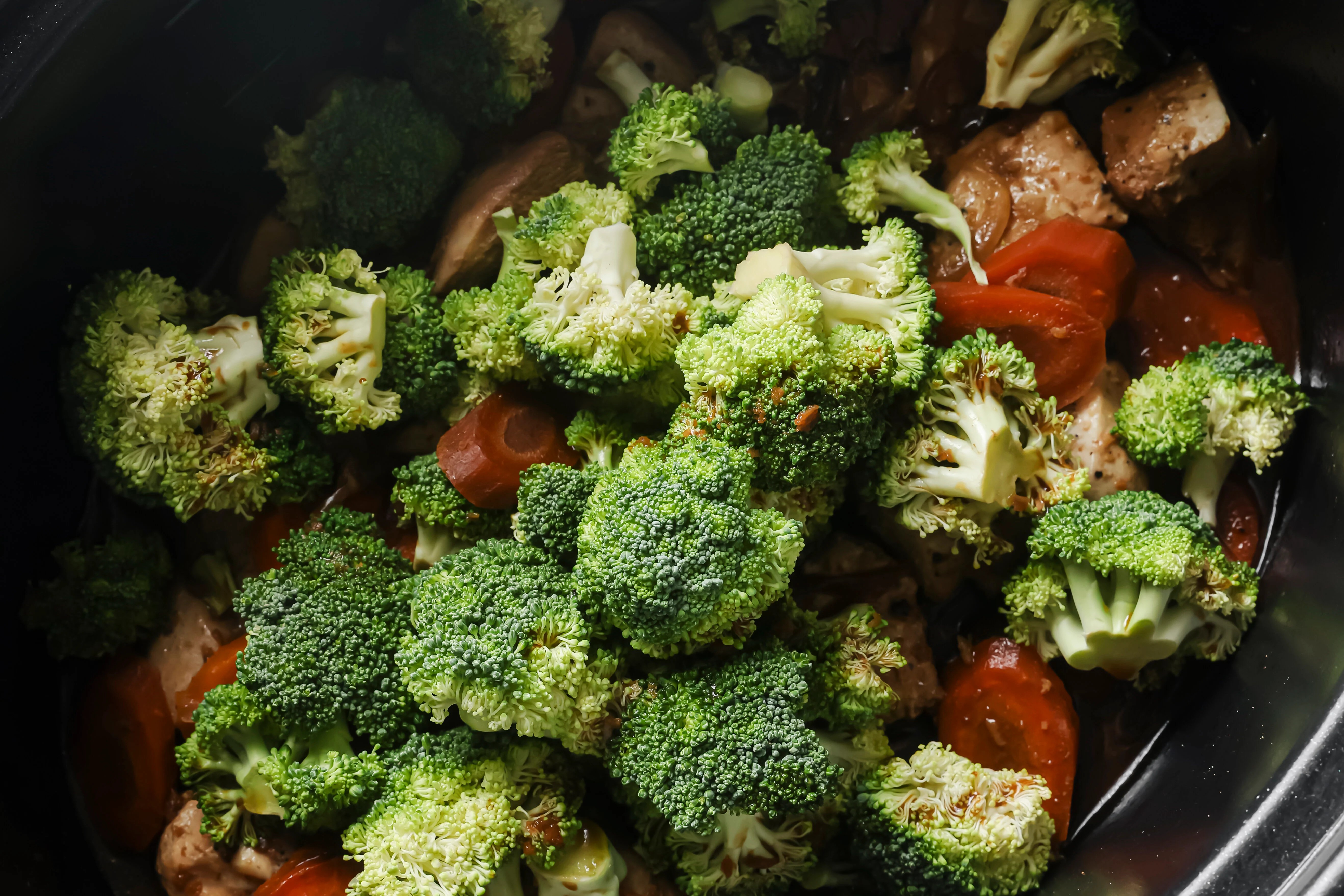Chicken and carrots cooked in a slow cooker with the sauce with fresh broccoli on top.