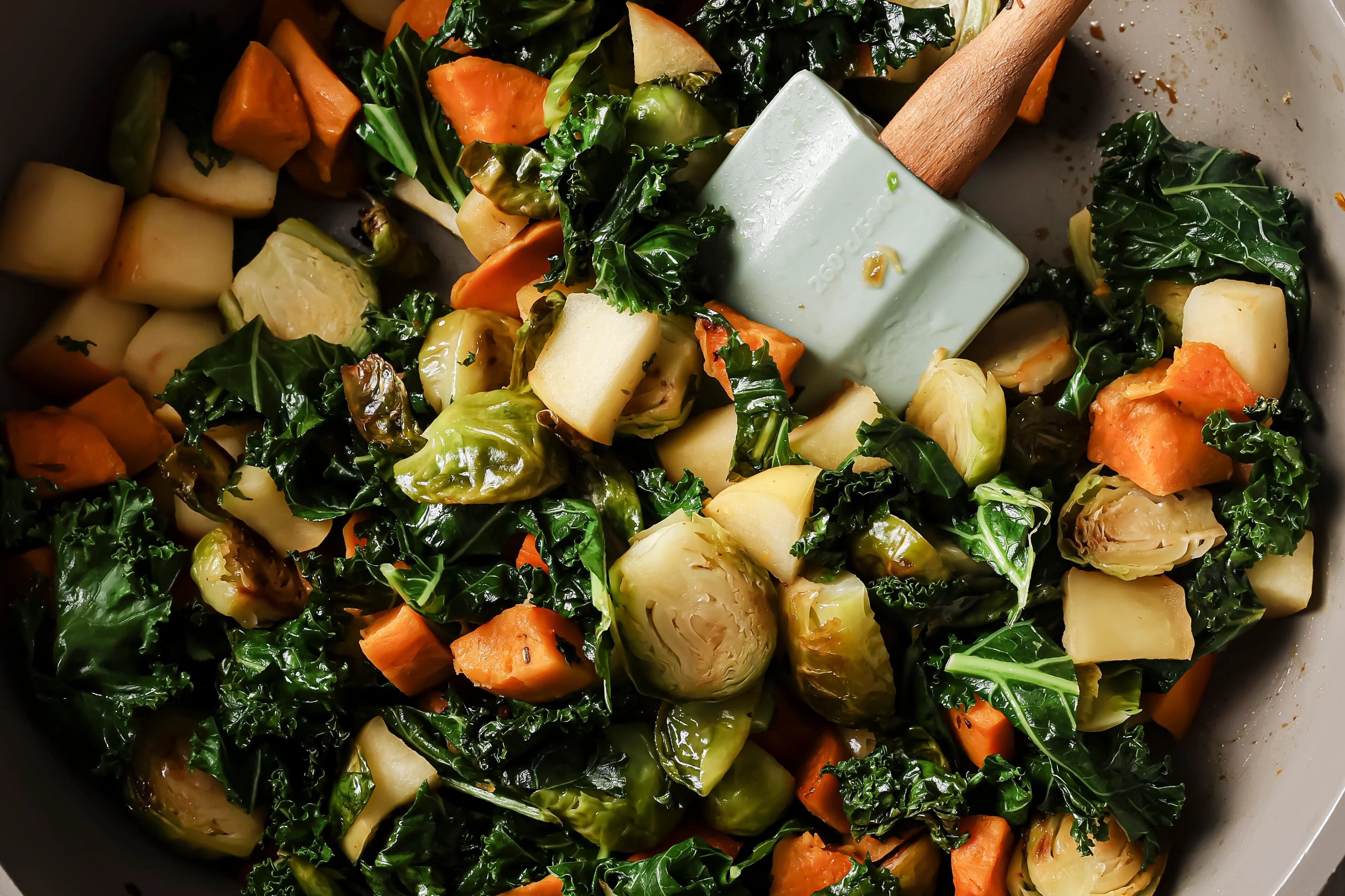 The kale and apples being added to the pan with other vegetables to saute.