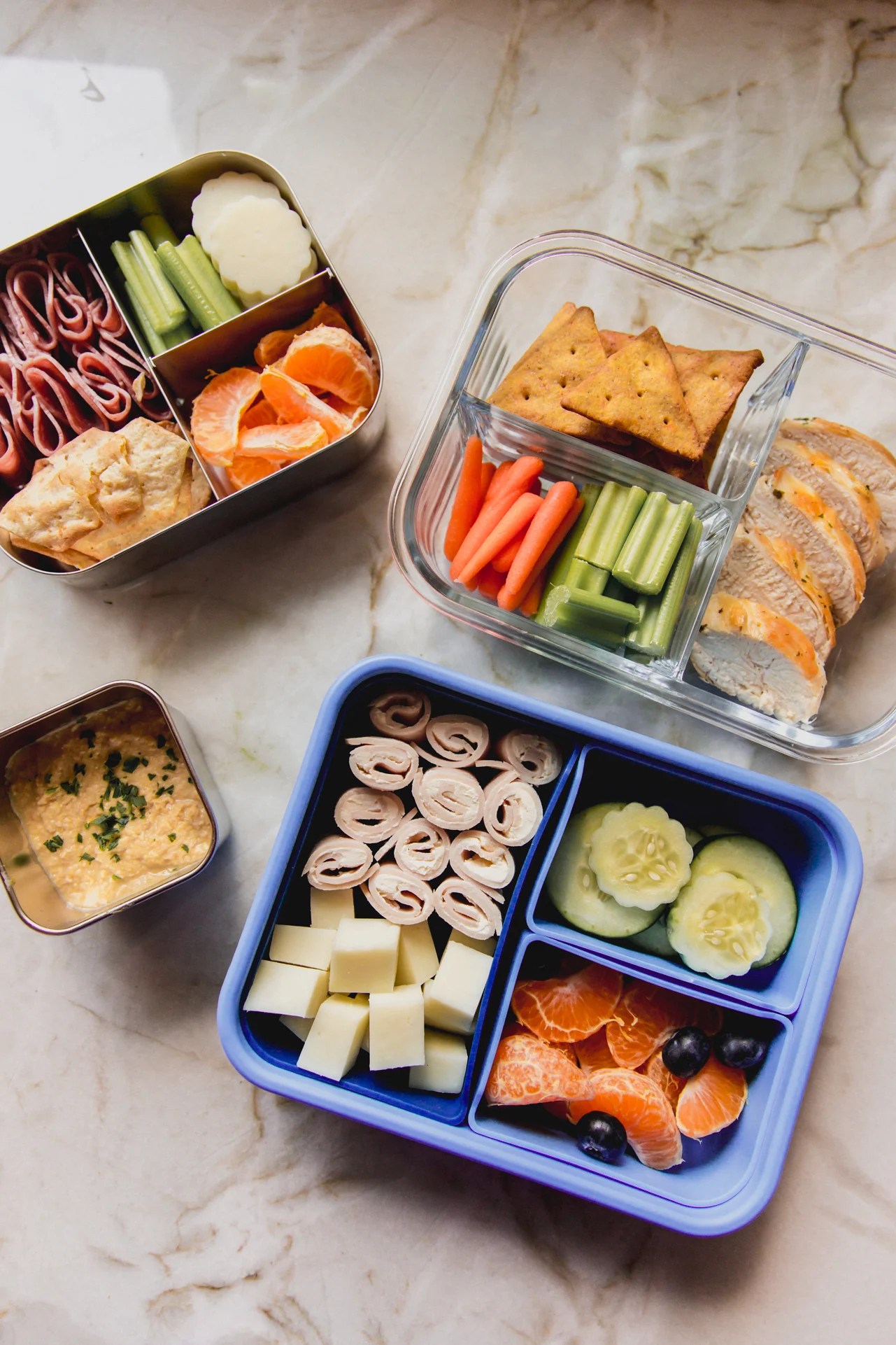 Three fully prepared kids lunch boxes with a side of hummus in a separate container. 