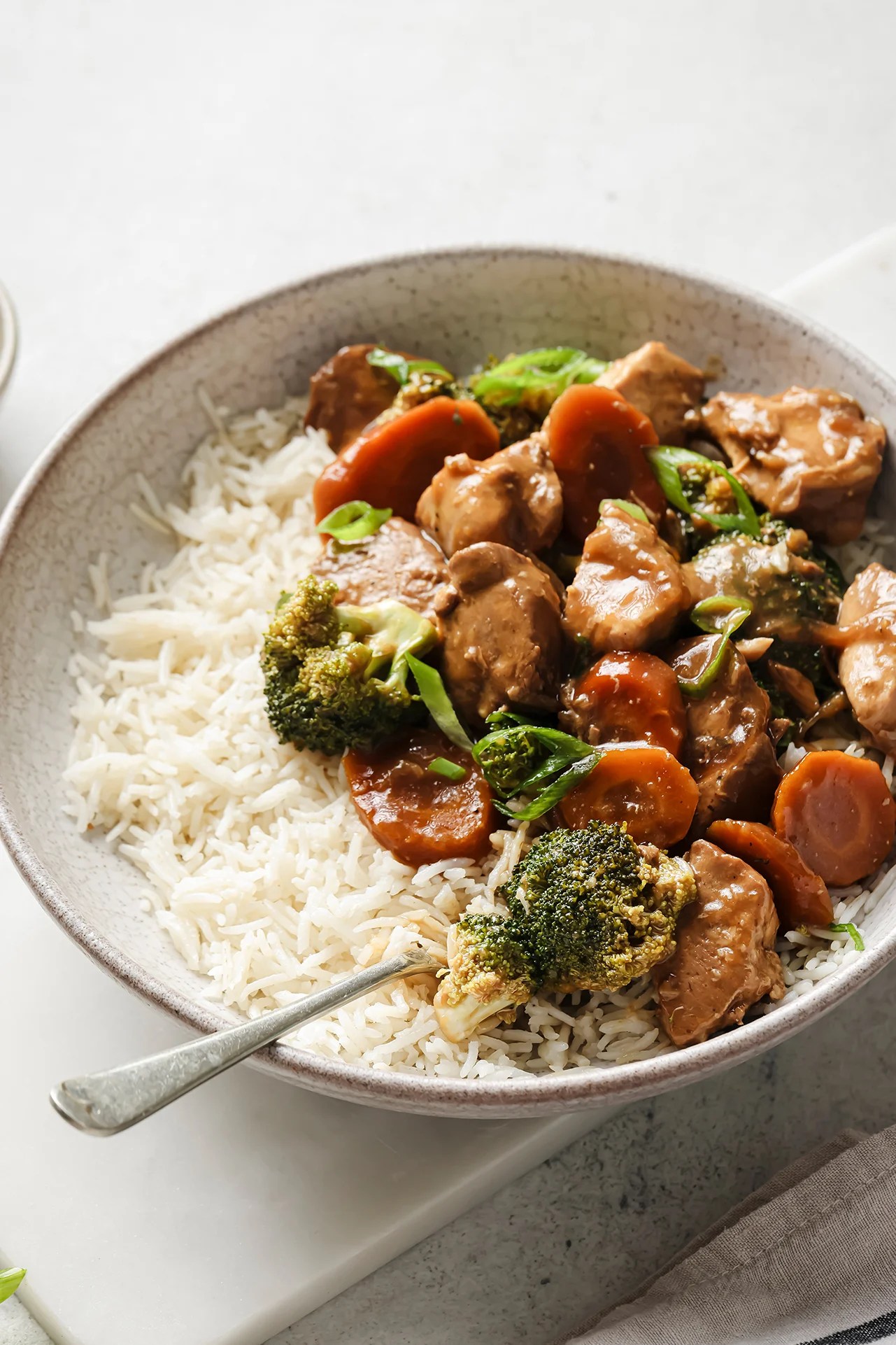 Slow cooker chicken and broccoli in a bowl with a side of rice, topped with chopped green onion.