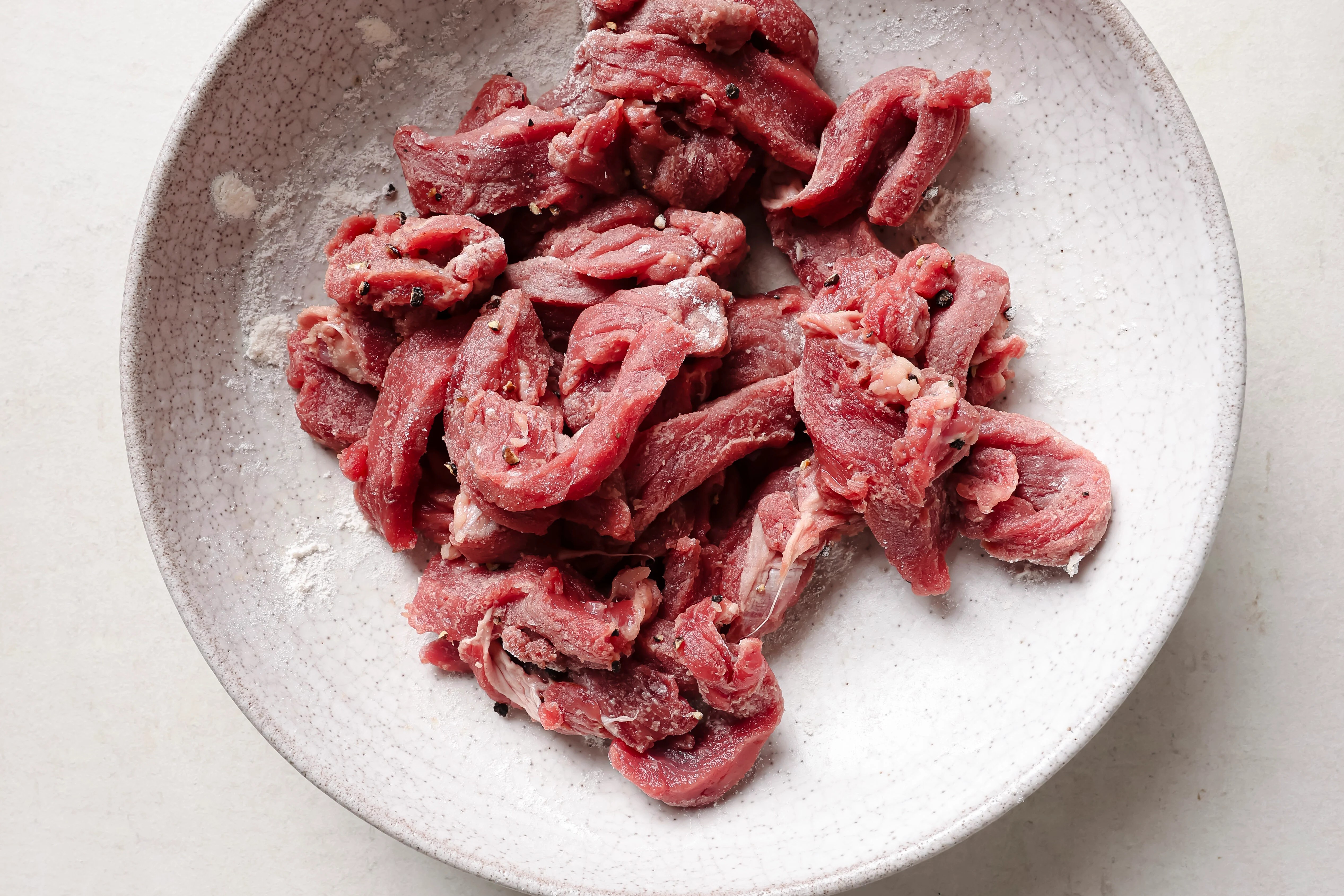 A white bowl with cut up beef being coated in arrowroot starch.