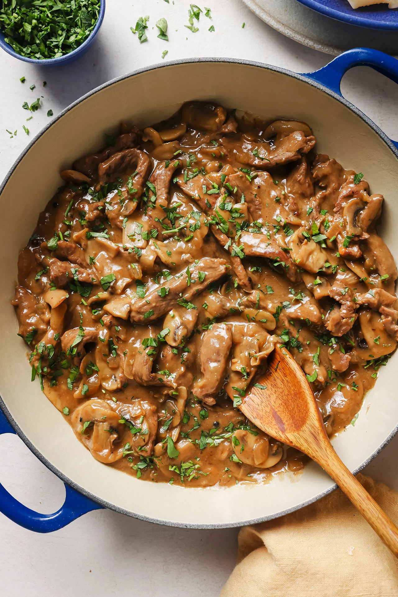 A Dutch oven filled with beef stroganoff after cooking with a wooden spoon in it.