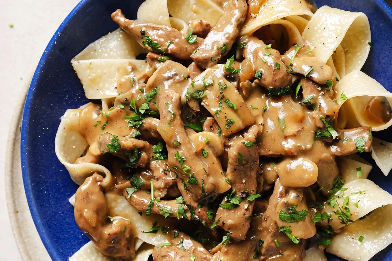 A serving of beef stroganoff over pasta in a blue bowl.