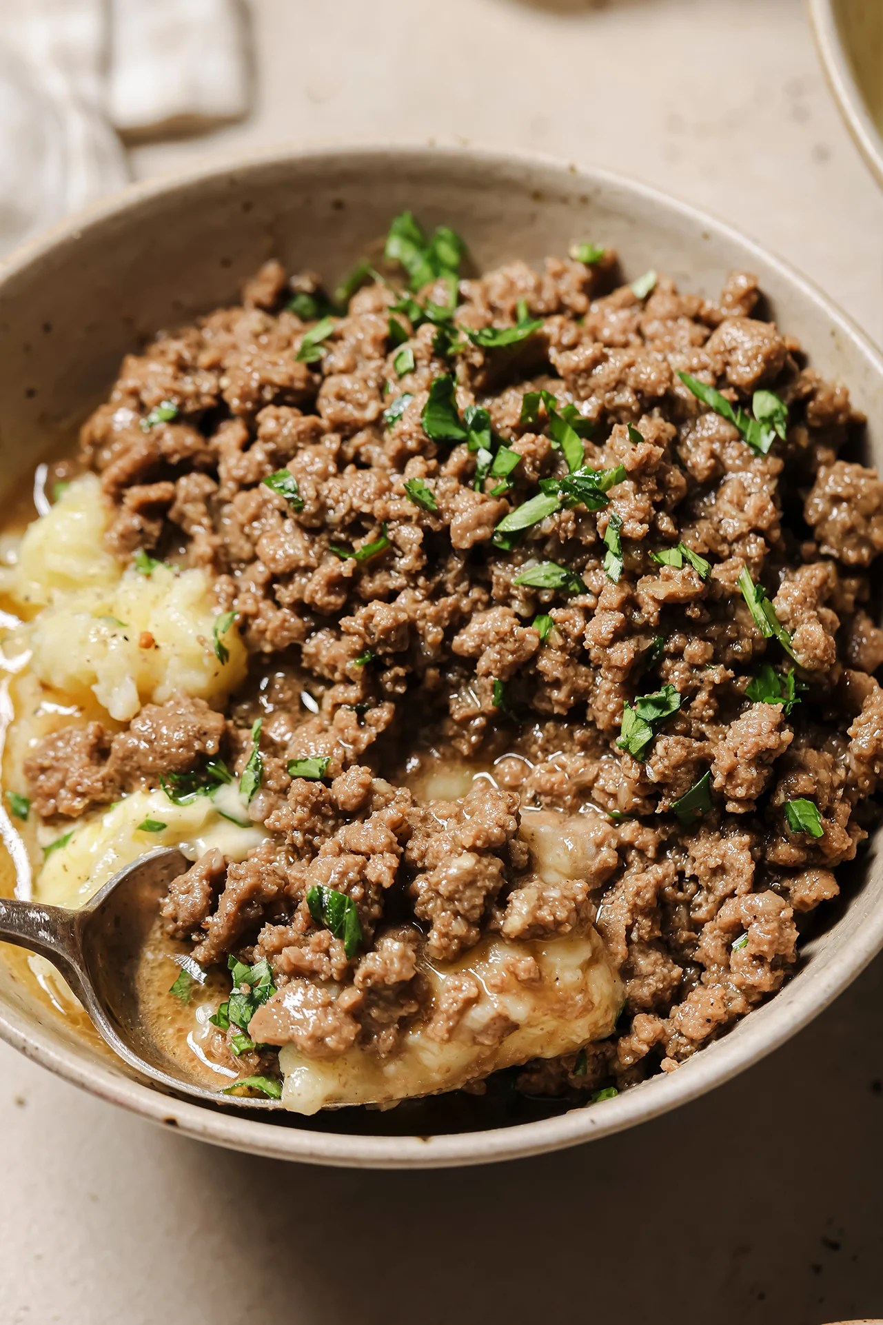 Ground beef and gravy served over mashed potatoes in a bowl.