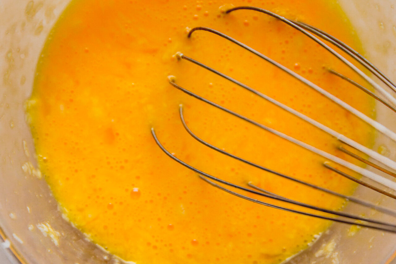 A whisk in a glass bowl mixing the eggs and cheese together.