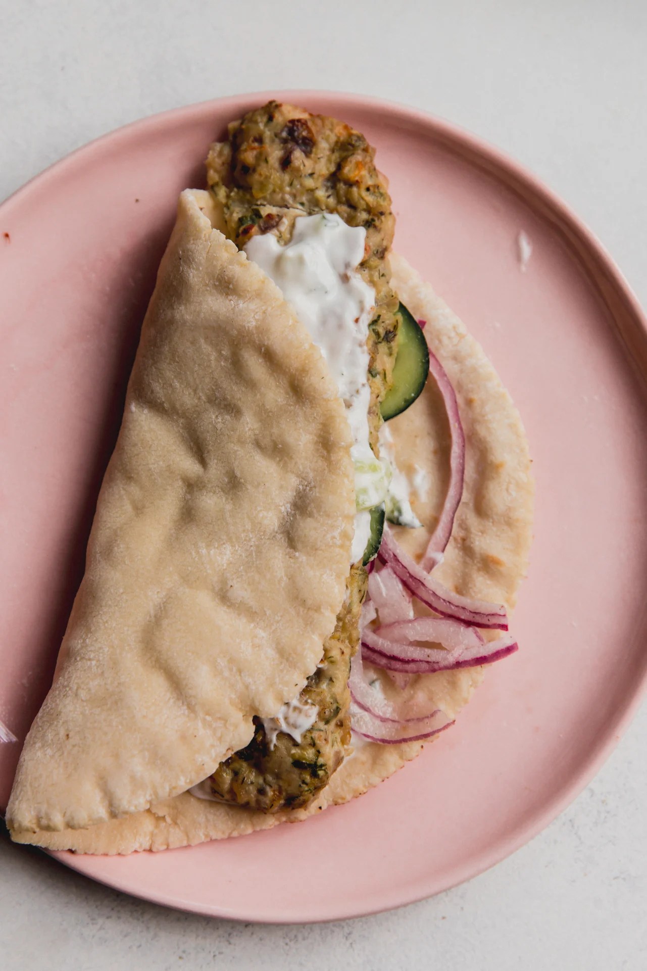 A ground chicken sheet pan kebab wrapped in a pita with cucumber, onion, and sauce.
