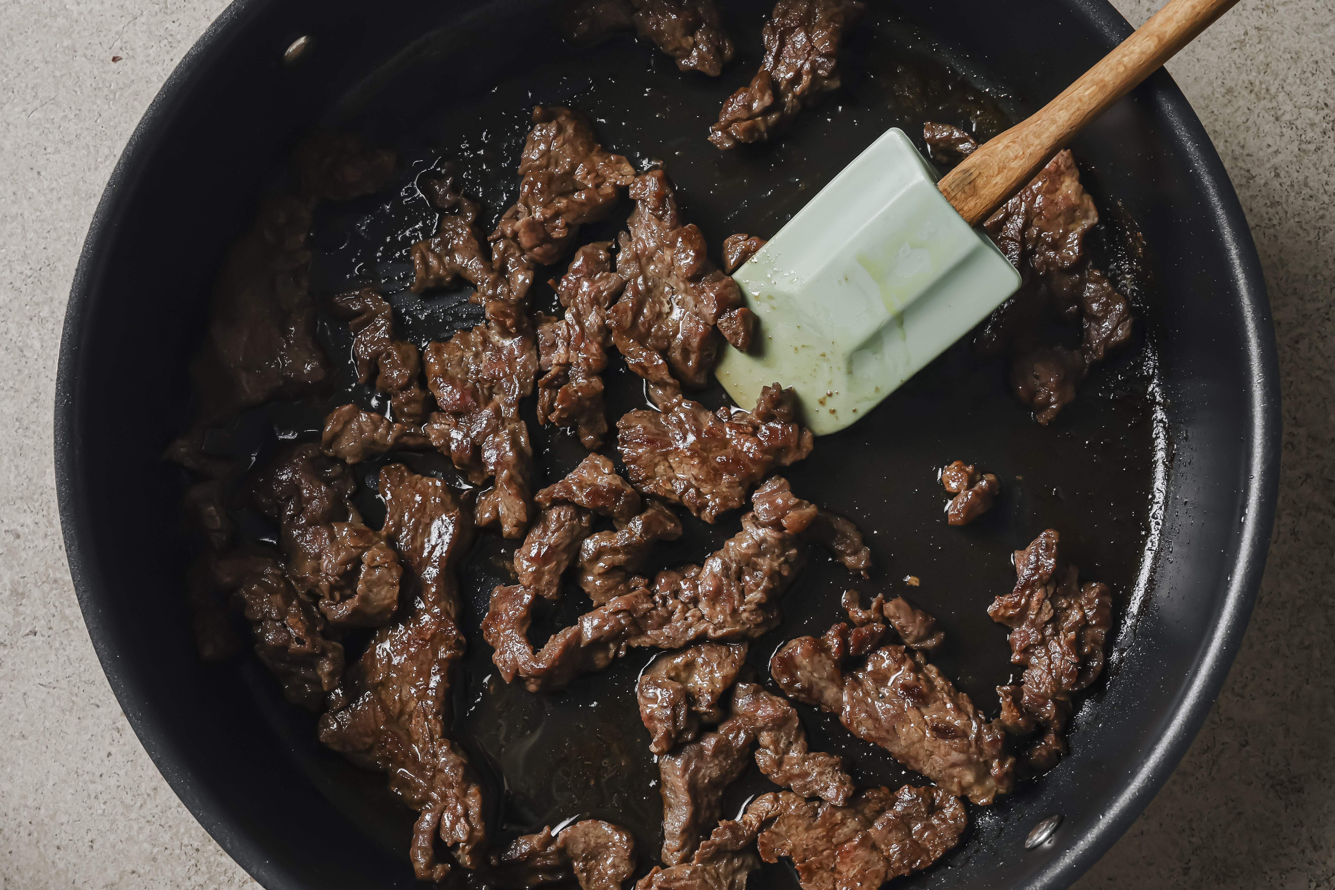 Sliced flank steak cooking in a large pan with a spatula.