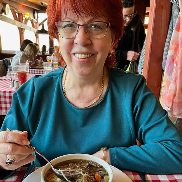 Woman with red hair and blue shirt eating a bowl of soup