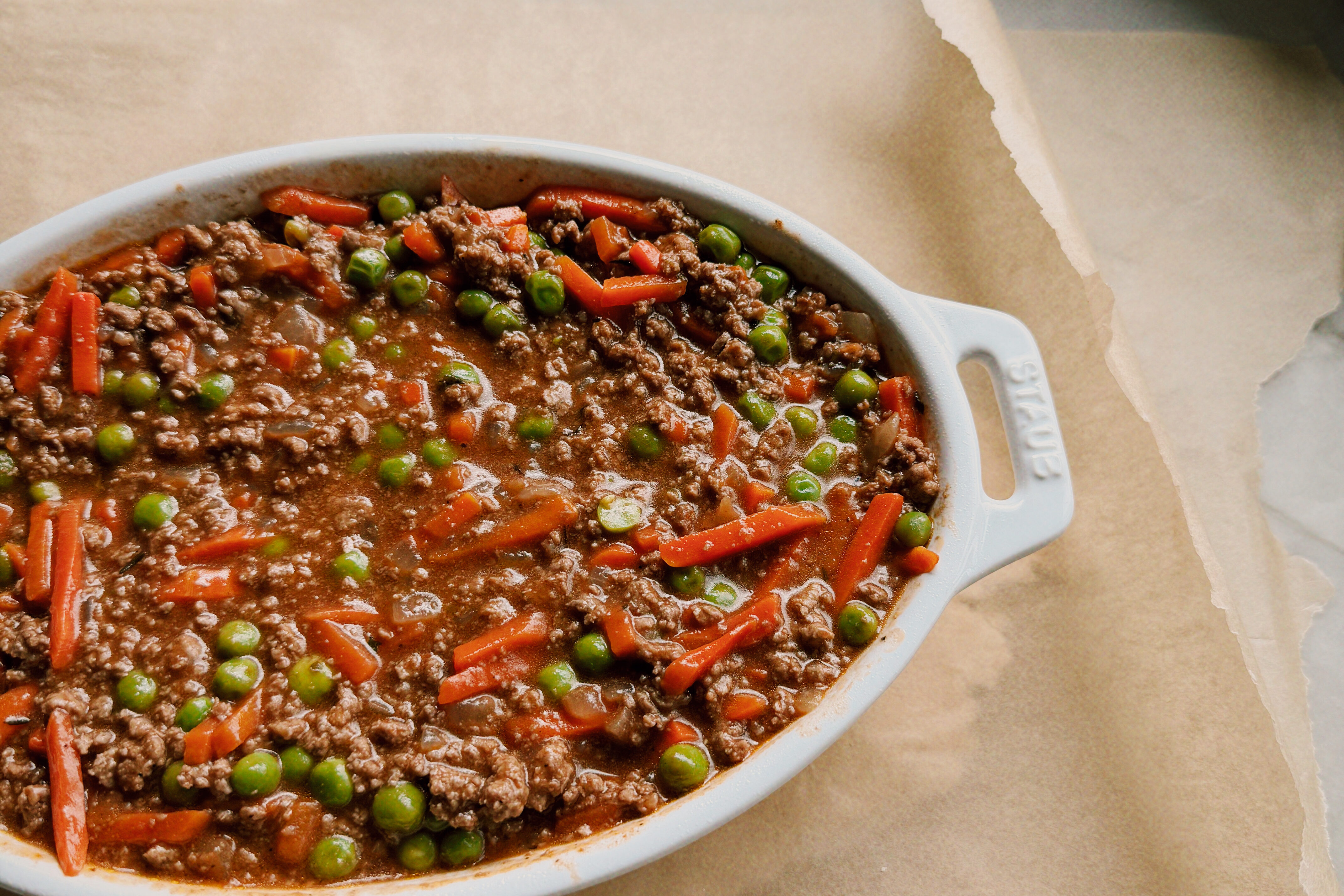 A white staub pan with the ground beef mixture filling it sitting on top of dough and parchment paper.