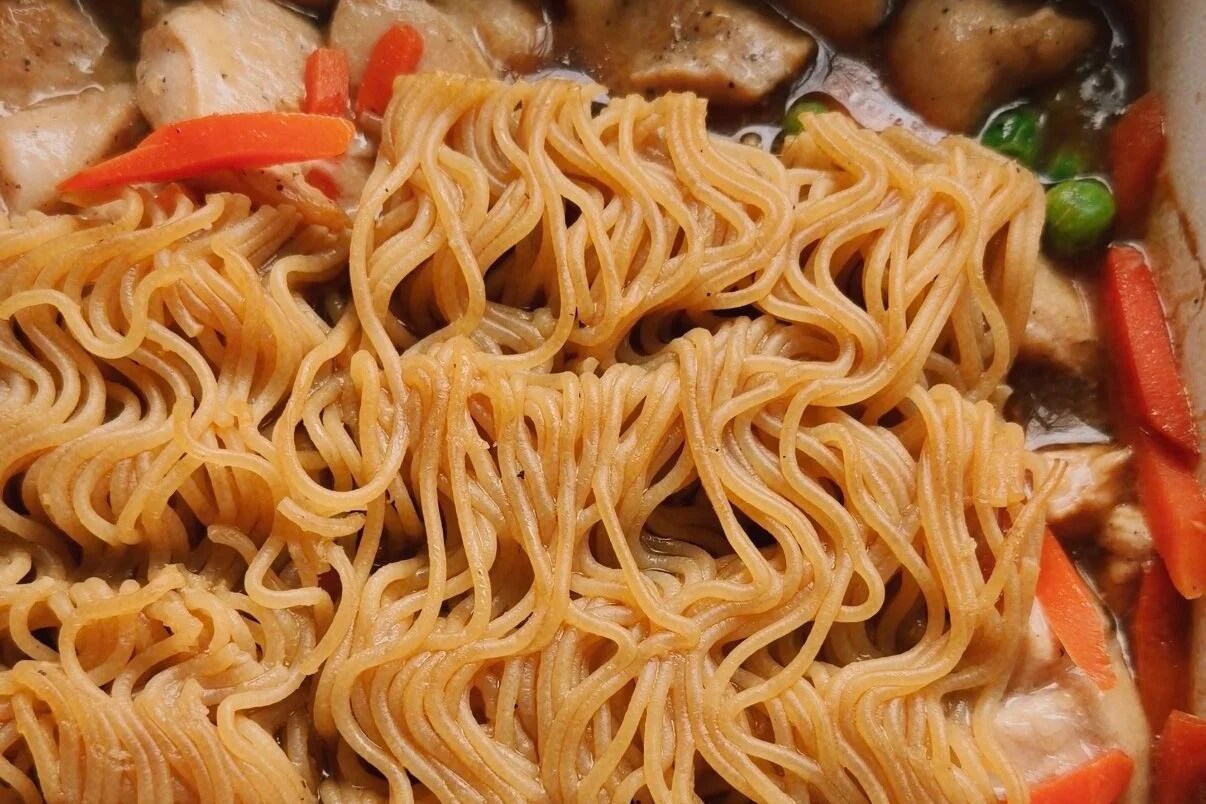 Partially cooked ramen bricks in a cassrole dish with veggies and chicken.